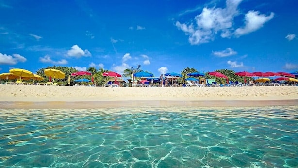 A beach with clear turquoise water, white sand, and colorful umbrellas. - Chambre dans Villa Casa Blue, piscine, vue mer (Cole Bay)