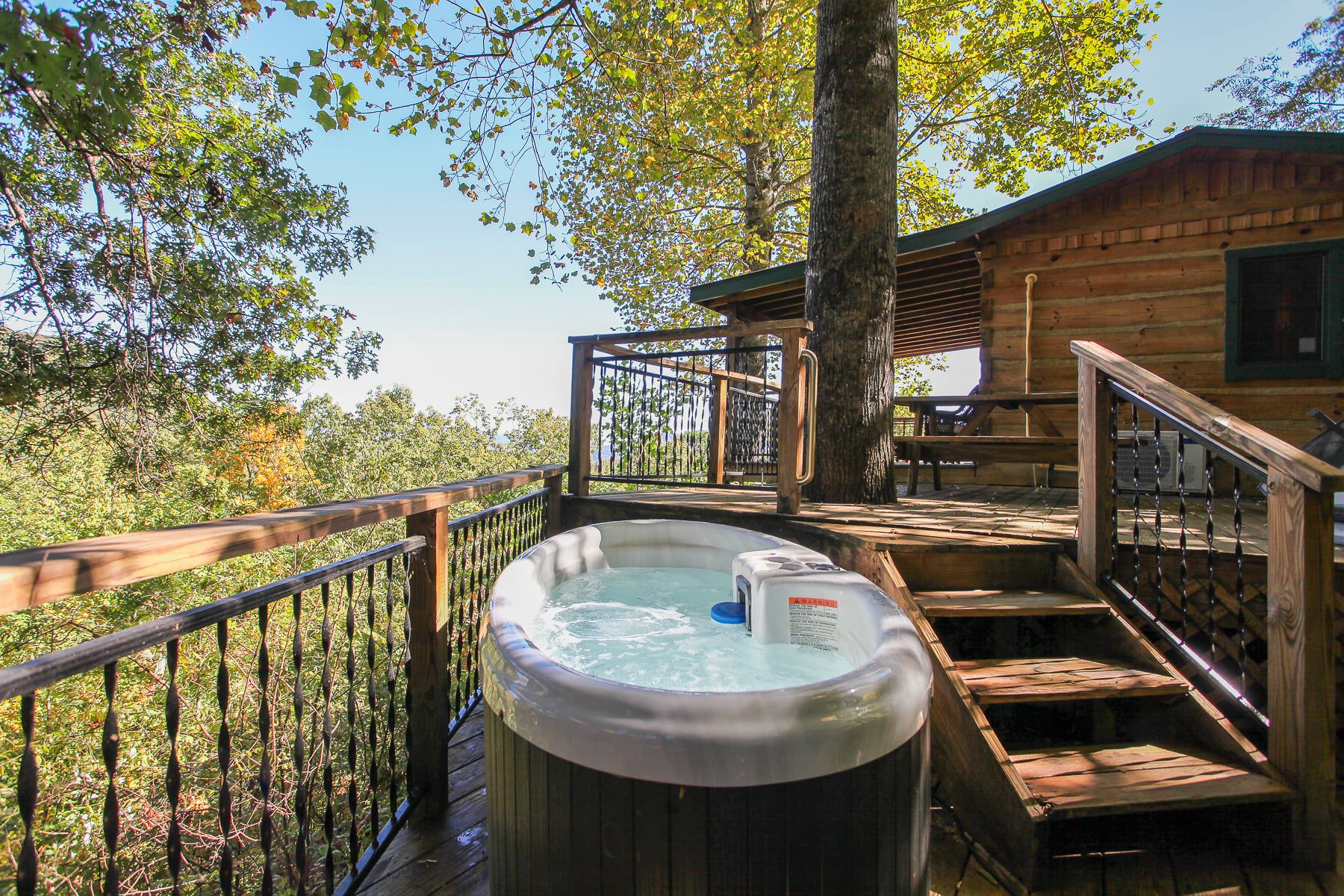 A wooden deck with a hot tub, wooden stairs, and a wooden cabin in the background.