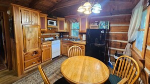 Une cuisine rustique aménagée dans une cabane en bois, avec une table ronde en bois, des placards en bois, un réfrigérateur et un four à micro-ondes.