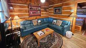 L’intérieur chaleureux d’un chalet en bois comprend un canapé en cuir bleu, une table basse en bois et un ventilateur de plafond.