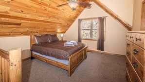 Un dormitorio con techo de madera, una cama, un aparador y una ventana.