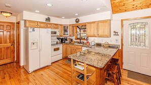A kitchen with wooden cabinets, a white refrigerator, a microwave, a stove, and a granite countertop.