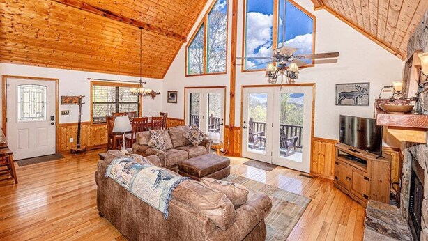 A spacious living room with a high ceiling, large windows, a fireplace, and a television.
