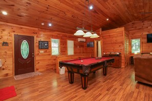 A wooden cabin interior with a pool table, a sofa, and a door with a decorative glass panel.