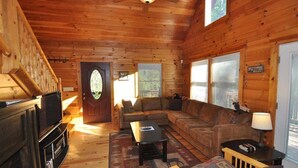A wooden cabin interior with a living room, sofa, coffee table, and a television. - Experience mountain living at The Fiddlers Green (Bryson City)