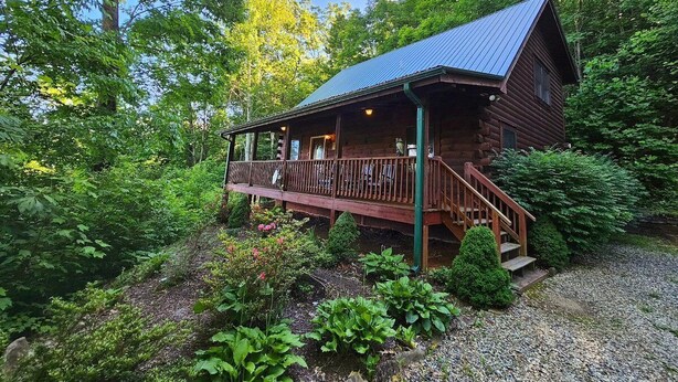 A rustic cabin with a porch, surrounded by dense greenery. - Experience mountain living at The Fiddlers Green (Bryson City)