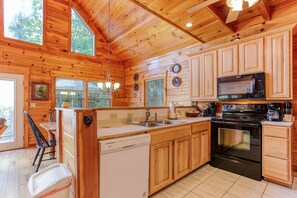 A wooden cabin interior with a kitchen featuring a dishwasher, stove, microwave, and wooden cabinets. - Experience mountain living at The Fiddlers Green (Bryson City)