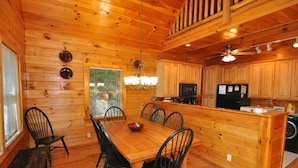 A wooden cabin interior with a dining area, kitchen, and a small balcony. - Experience mountain living at The Fiddlers Green (Bryson City)