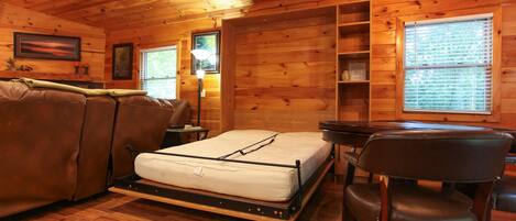Interior de uma cabana de madeira com uma cama, um sofá, uma escrivaninha e uma cadeira.