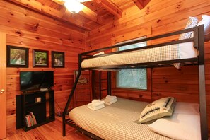 A bunk bed with a checkered bedspread, a television on a stand, and framed pictures on the wall. - Experience mountain living at The Fiddlers Green (Bryson City)