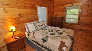 A wooden cabin bedroom with a bed, two windows, a nightstand, and a dresser. - Experience mountain living at The Fiddlers Green (Bryson City)