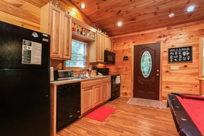 A wooden cabin interior with a kitchen area featuring a refrigerator, microwave, stove, and wooden cabinets.