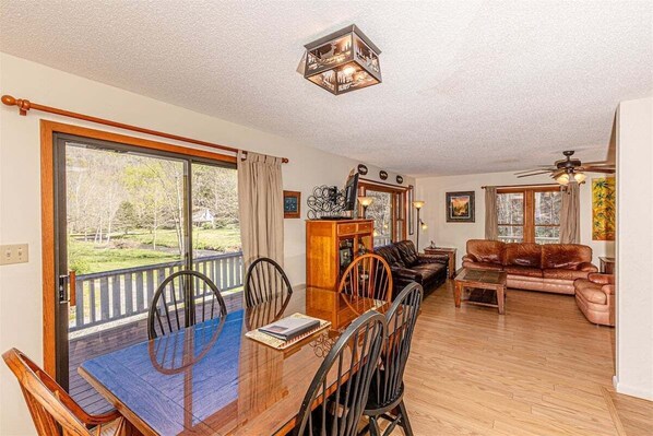 A spacious living room with a wooden dining table, leather sofa, and a balcony with a view of the outdoors.