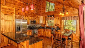 A wooden cabin kitchen with a central island, stainless steel appliances, and a dining area. - Shooting Star Ridge: Mountain View Cabin Near Cherokee with Hot Tub (Whittier)