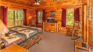 A log cabin bedroom with a bed, dresser, rocking chair, and a television. - Shooting Star Ridge: Mountain View Cabin Near Cherokee with Hot Tub (Whittier)