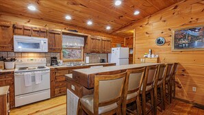 Cocina de cabaña de madera con una isla central, armarios de madera, microondas, estufa, refrigerador y un cuadro en la pared.