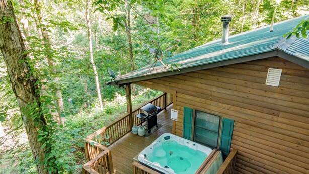 Una cabaña de madera con un jacuzzi en una terraza rodeada de árboles.