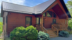 Une cabane en bois avec un toit en pente, une véranda à l’avant et une allée gravillonnée.