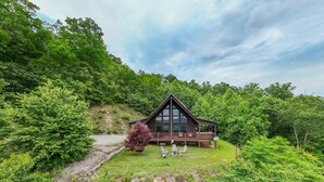 A cabin with a deck, surrounded by dense forest. - A Walk in the Clouds (Bryson City)