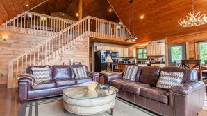 A spacious living room with a large brown leather sectional sofa, a glass coffee table, and a wooden staircase leading to an upper level. - A Walk in the Clouds (Bryson City)