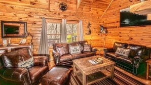 L’intérieur chaleureux d’un chalet avec des murs en bois, des canapés en cuir, une table basse en bois et un téléviseur fixé au mur.
