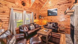 Un intérieur de chalet chaleureux avec des murs en bois, des canapés en cuir, une cheminée et une vue magnifique par les fenêtres.