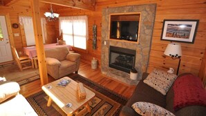 A cozy cabin interior with a stone fireplace, wooden walls, a dining area, and a sofa. - Cherokee Ridge Retreat (Whittier)
