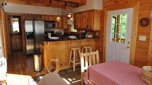 A cabin interior with a kitchen, dining area, and a door leading outside. - Cherokee Ridge Retreat (Whittier)