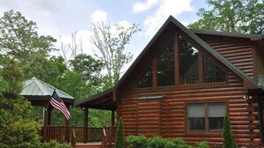A log cabin with a porch, a small gazebo with an American flag, and a well-maintained garden. - Cherokee Ridge Retreat (Whittier)