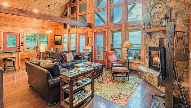 A cozy cabin interior with a large fireplace, wooden walls, and a high ceiling.