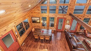 A wooden cabin with a dining area, large windows, and a cozy seating area.