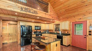 A spacious kitchen with wooden cabinetry, a central island with stools, and a red door.