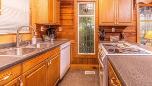 Una cocina tipo cabaña de madera con encimeras de granito, lavavajillas y estufa.