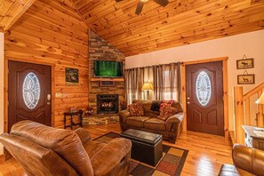 A cozy log cabin interior with a fireplace, leather furniture, and wooden walls.