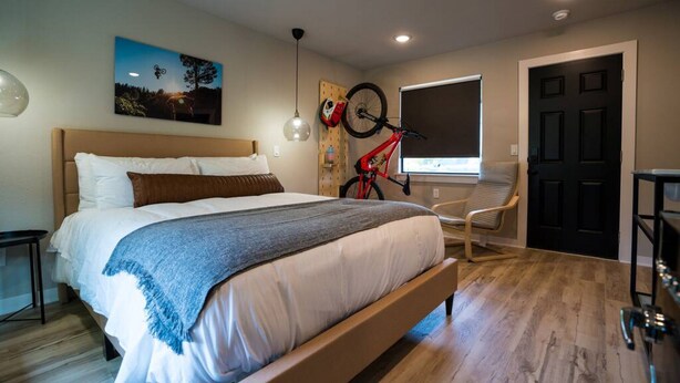 A bedroom with a bed, a bicycle, a window, and a door. - The Bike Inn #3, Mt Kessler, Single Room (Bentonville)