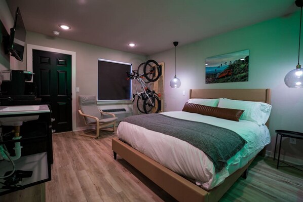 A bedroom with a bed, a desk, a chair, a bicycle, and a window.