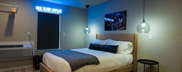 Une chambre à coucher avec un lit, un climatiseur fixé au mur, un néon et un tableau sur le thème du vélo.