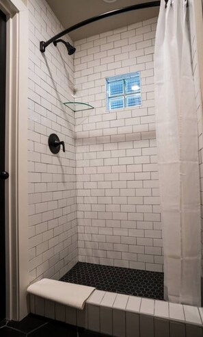 Un espace douche avec des murs recouverts de carreaux blancs, une étagère en verre et un banc.