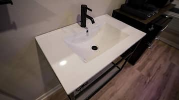 A white sink with a black faucet in a room with wooden flooring and a black cabinet.