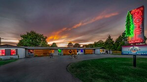 Un motel avec une enseigne au néon, un espace réservé au stationnement des vélos et un coucher de soleil en arrière-plan.