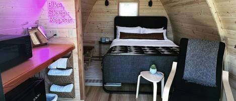 Un dormitorio acogedor en el ático con cama, una mesita, una silla y un escritorio con microondas.