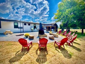 A rustic outdoor seating area with red Adirondack chairs, a stone fire pit, and a covered pavilion. - The Bike Inn #14, Buffalo River Cabin (Bentonville)