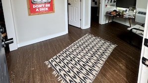 Un pasillo con suelo de madera, alfombra estampada, un cartel de Buda, una lámpara en el techo y un televisor montado en la pared.