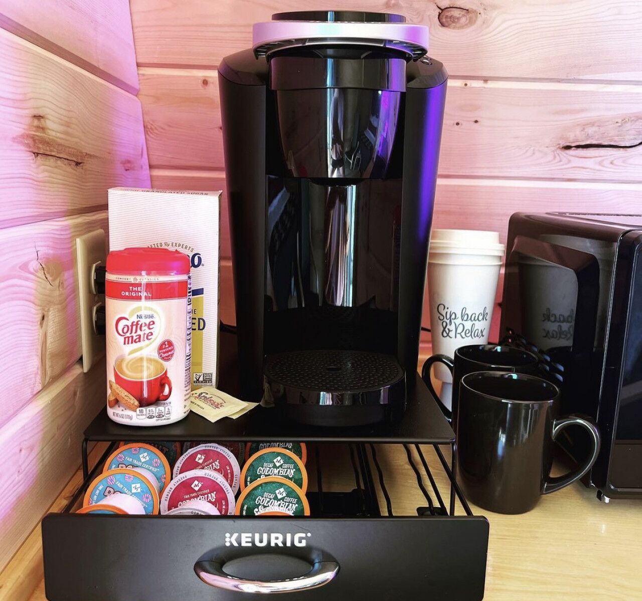 A Keurig coffee maker, a Nespresso coffee pod, a coffee mug, and a coffee cup on a wooden table.
