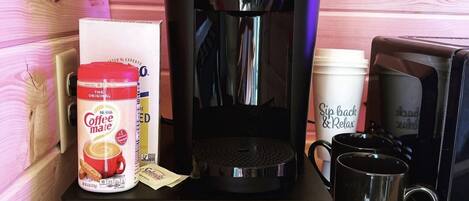 A Keurig coffee maker, a Nespresso coffee pod, a coffee mug, and a coffee cup on a wooden table.