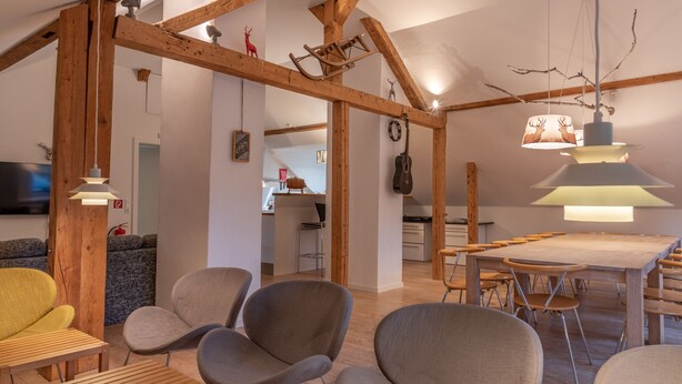 A spacious living area with wooden beams, a dining table, and modern furniture.