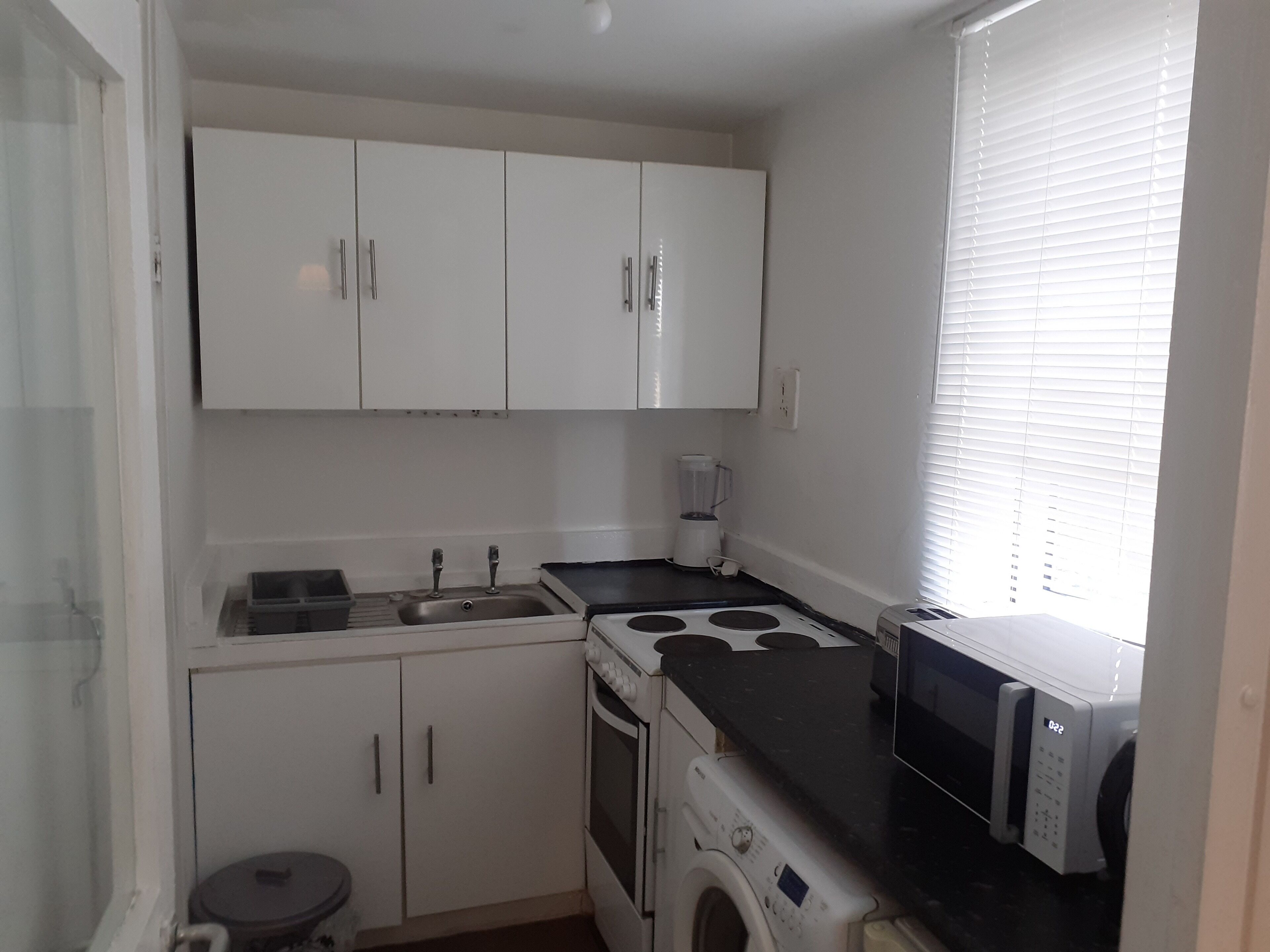 A compact kitchen with white cabinets, a sink, a stove, a microwave, and a washing machine.