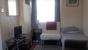 Une petite chambre d’hôtel, de taille réduite, comprenant un lit simple, un bureau avec un ordinateur, une chaise et un canapé.