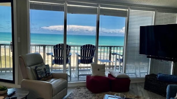 Ein Wohnzimmer mit einem großen Schiebeglasfenster, das auf einen Balkon mit Blick auf den Strand führt.