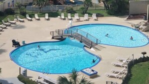 Ein Poolbereich mit zwei großen Pools, einer Spielanlage für Kinder und Liegestühlen.